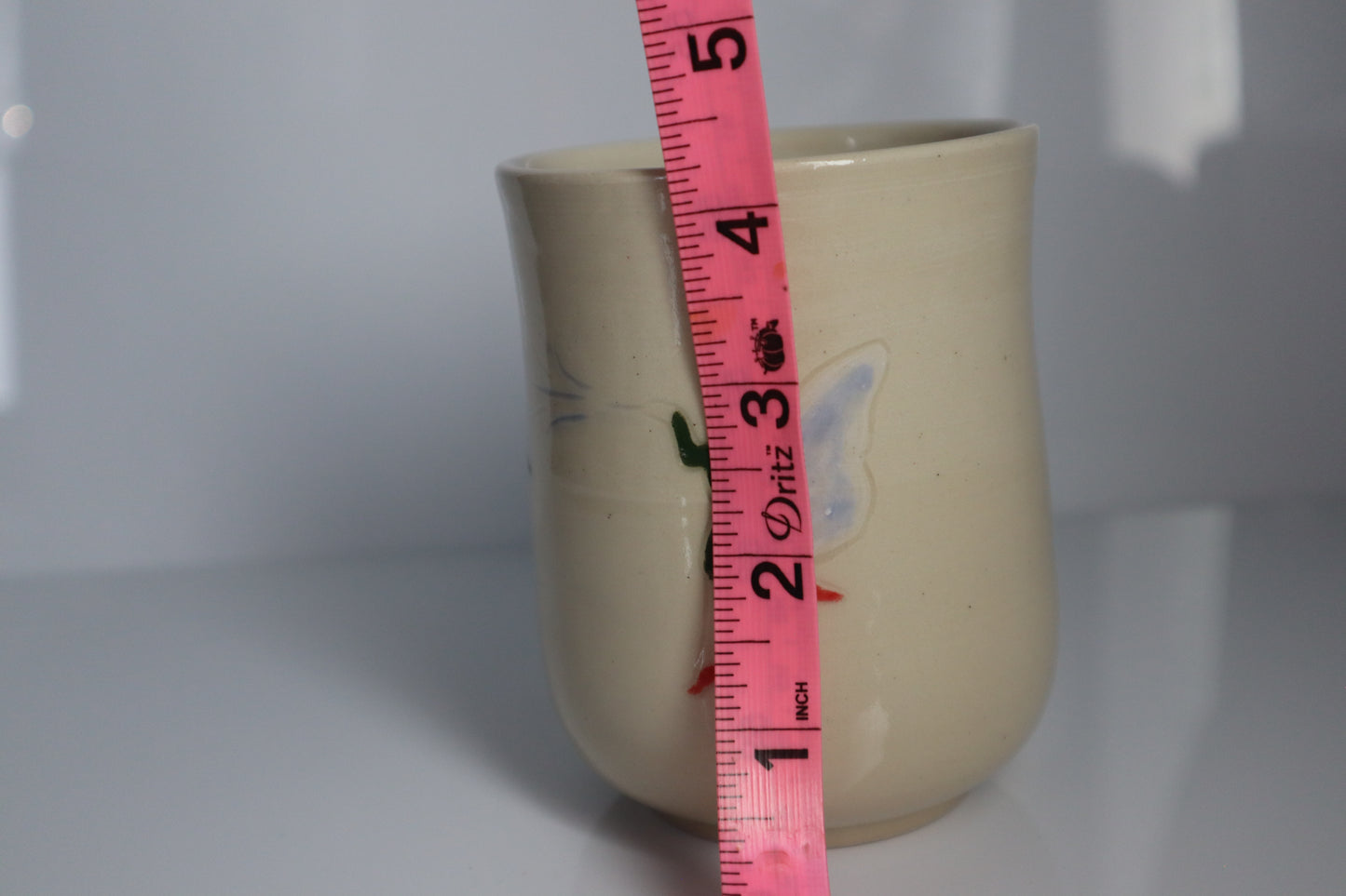 Ceramic mug with a pink measuring tape showing its height against a white background