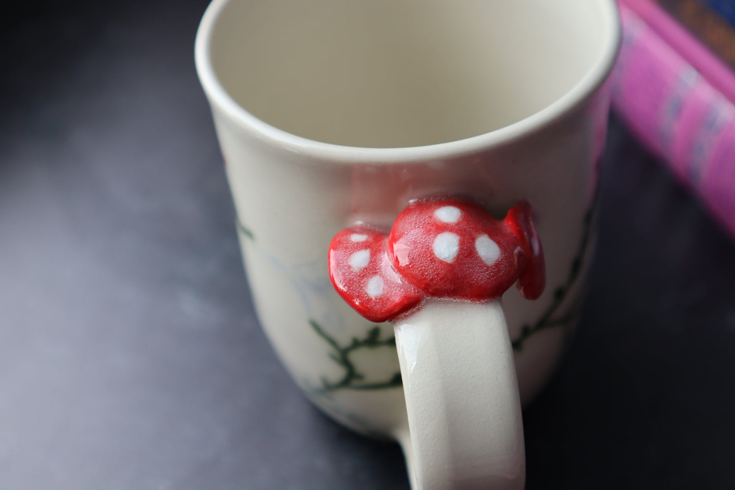 White mug with a red mushroom handle on a dark surface