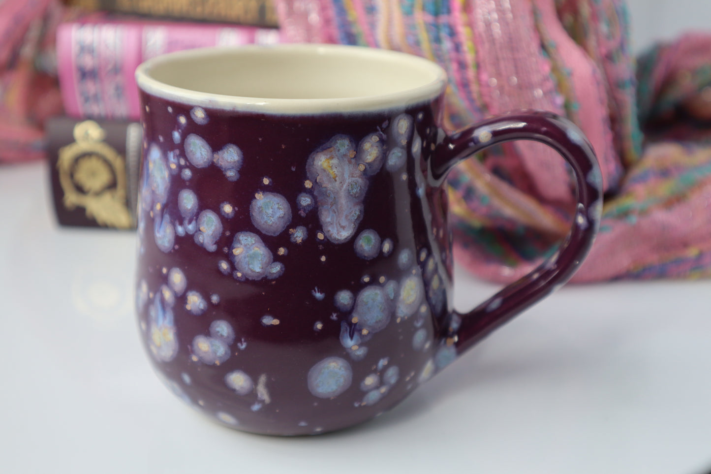 Mug with a purple and white abstract design on a white surface with colorful fabric in the background
