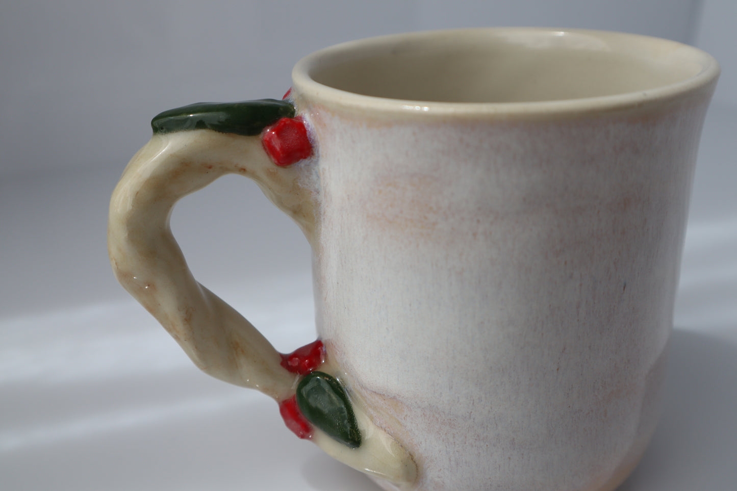Ceramic mug with decorative handle featuring red flowers and green leaves on a white background