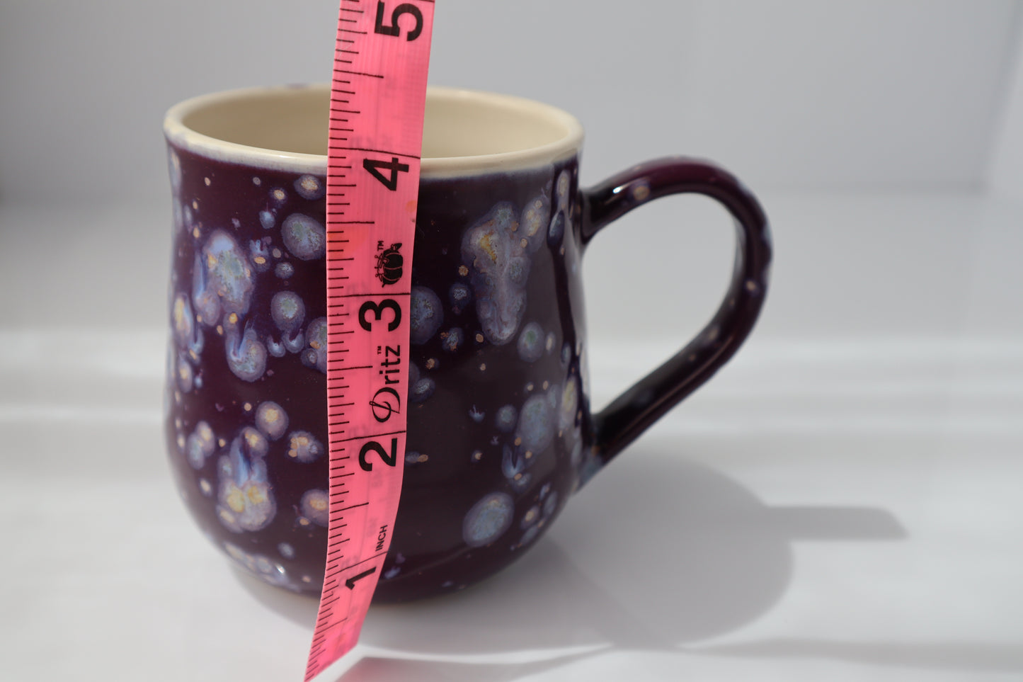 purple mug with a measuring tape showing its dimensions against a white background