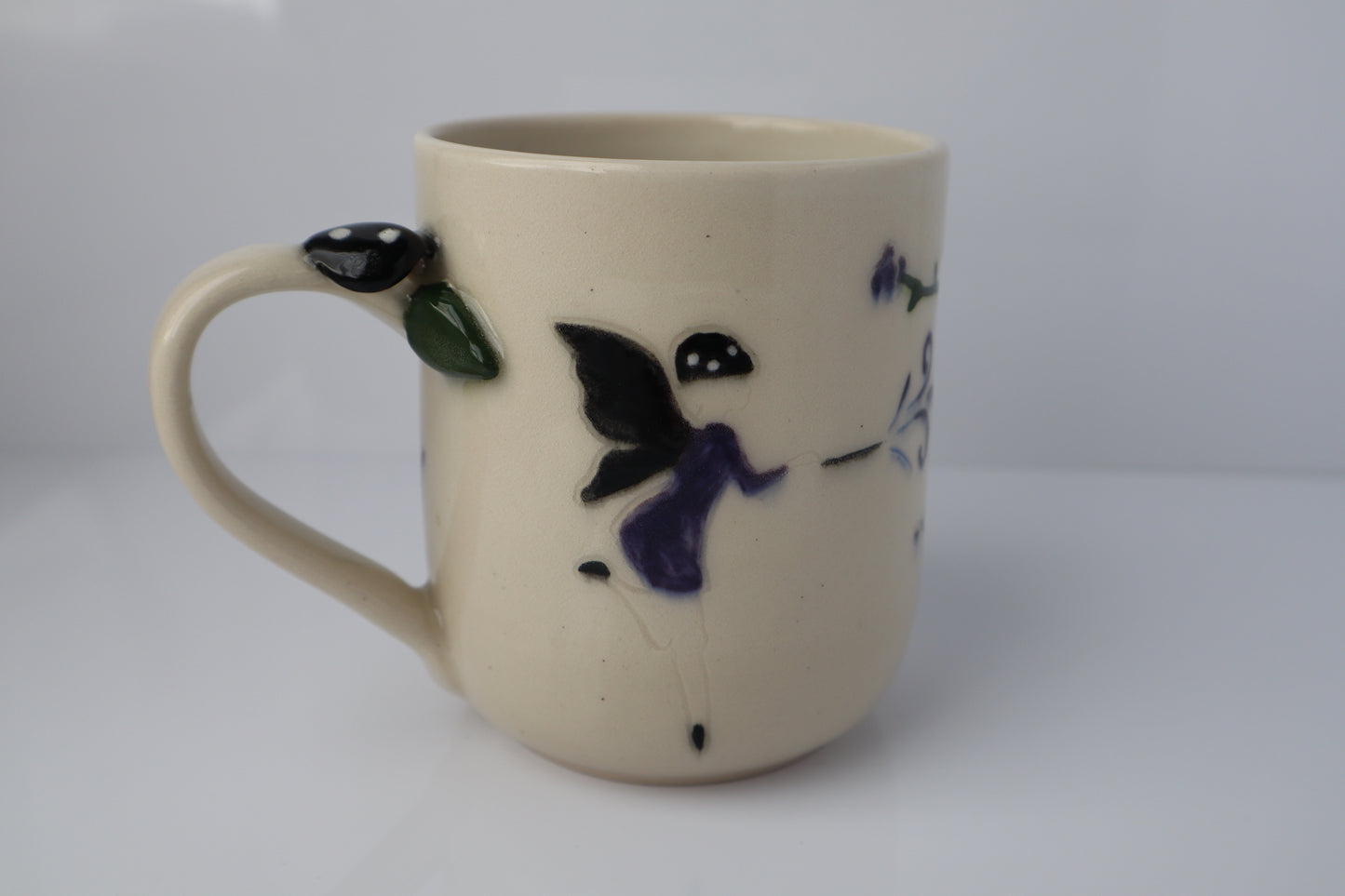 Beige ceramic mug with dark fairy and a black mushroom handle on a white background