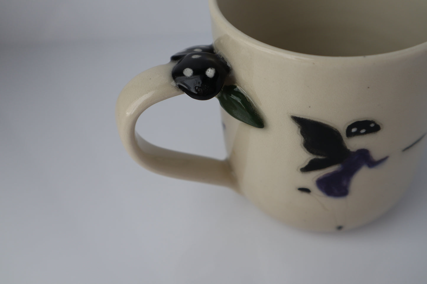 Ceramic fairy mug with black mushrooms on the handle on a white background