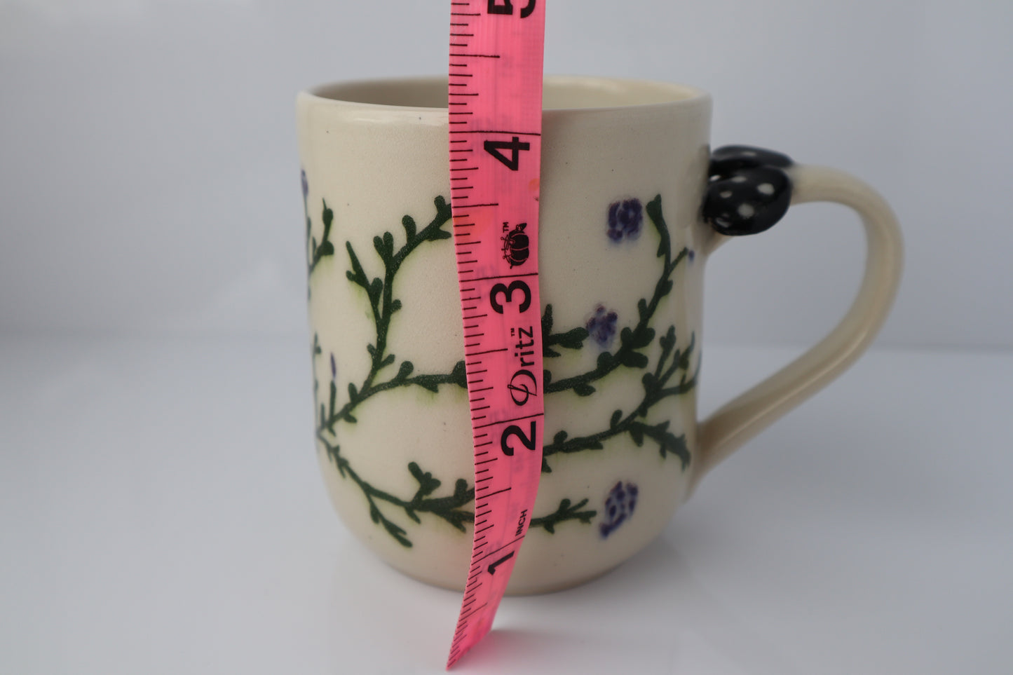 Mug with floral design and measuring tape for scale on a white background