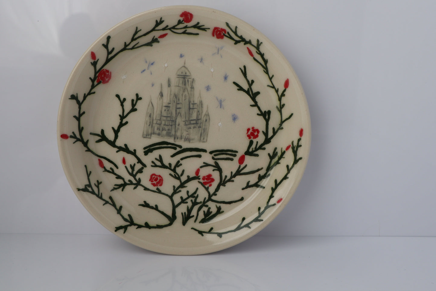 Decorative plate with a castle design and floral elements on a plain background