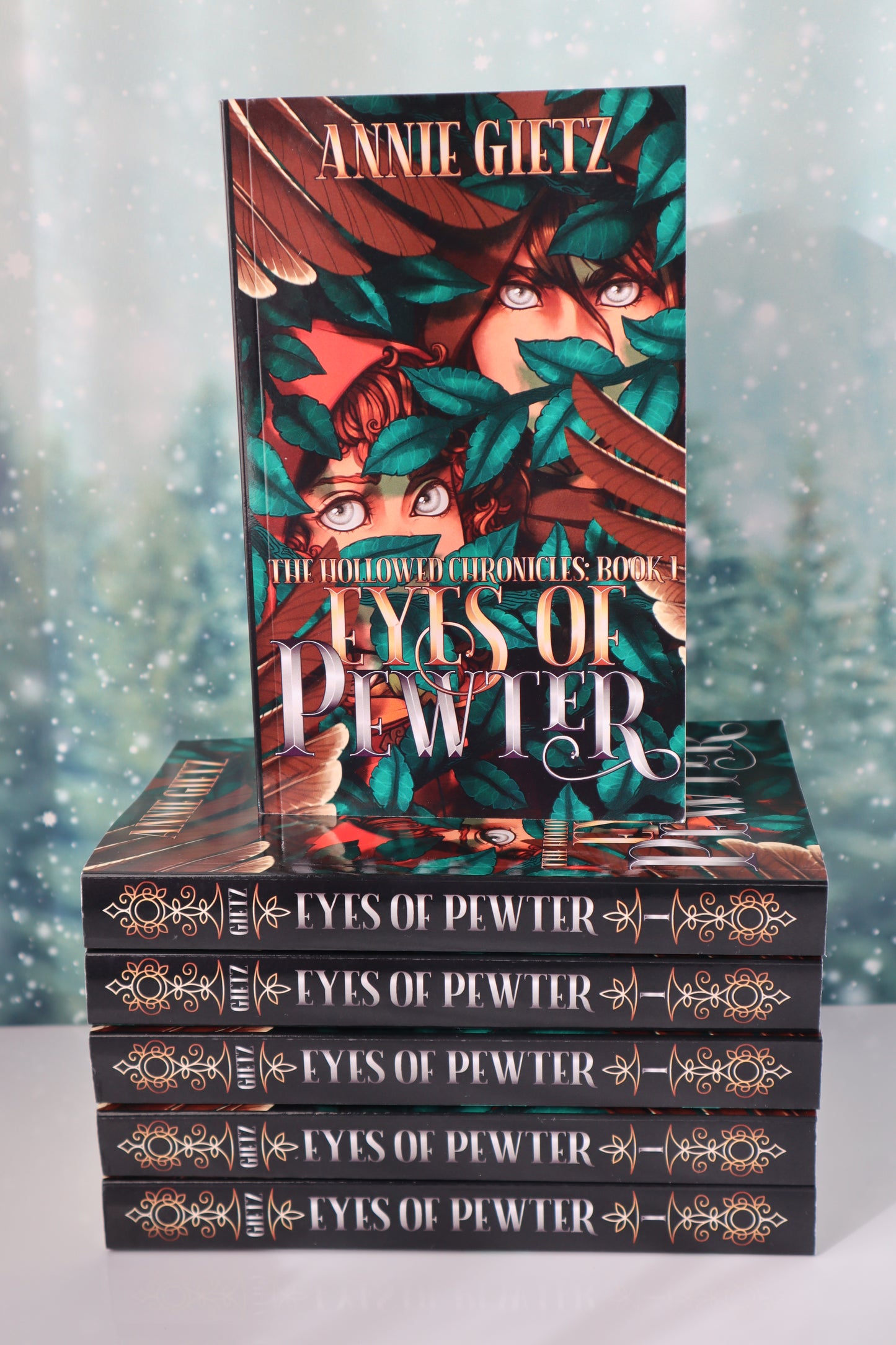 Book stack titled 'Eyes of Pewter' by Annie Gietz with one book on top of a stack of others with their spines out.