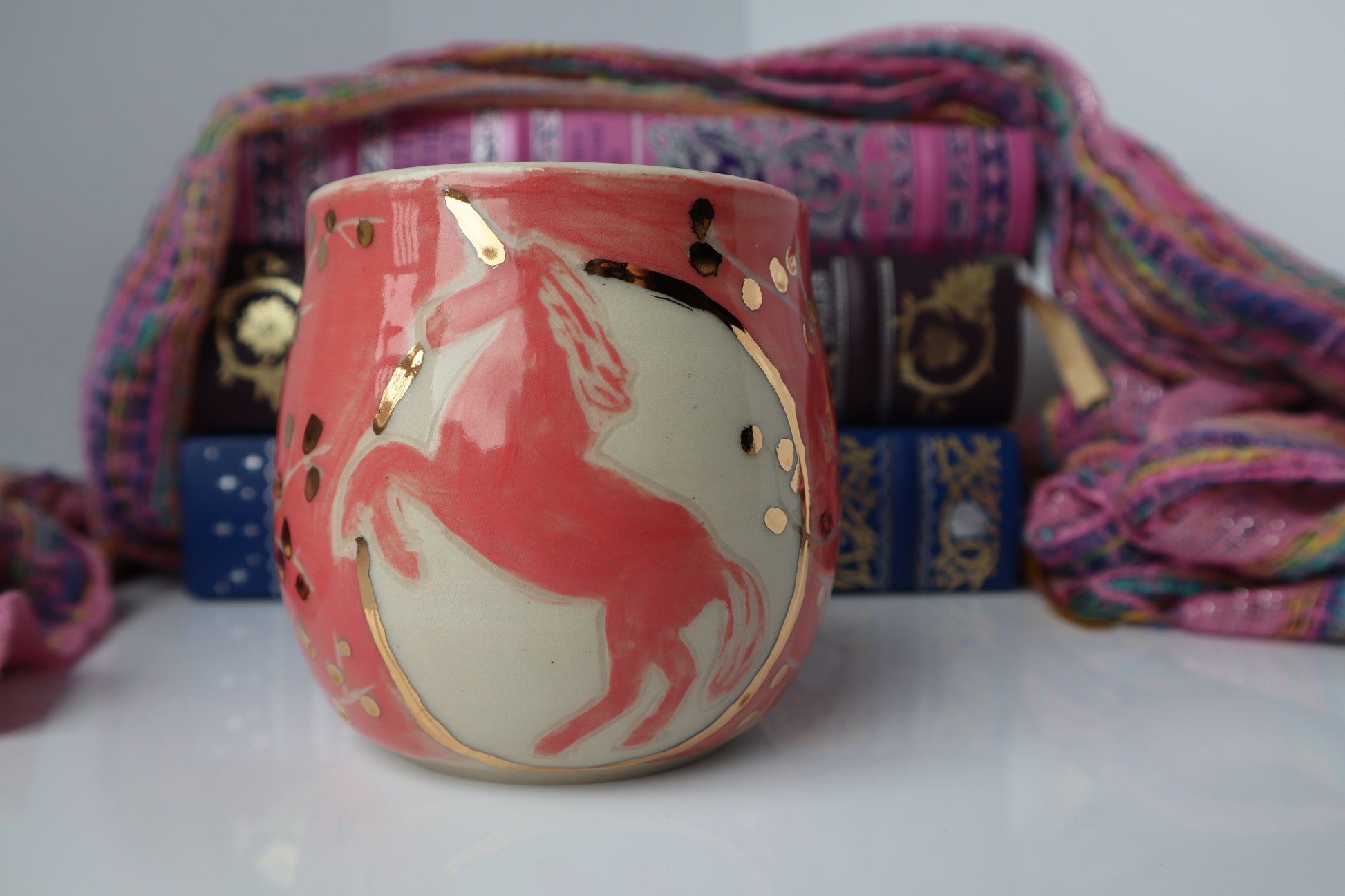 Ceramic mug with unicorn design in gold with colorful fabric in the background