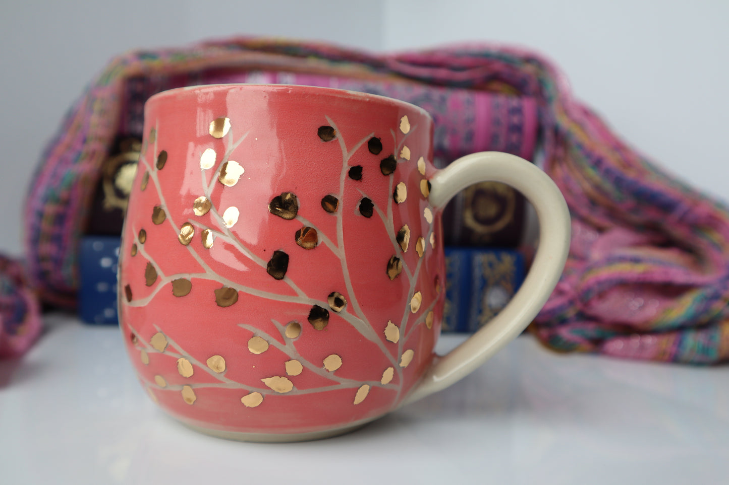Pink mug with gold patterns with colorful fabric in the background