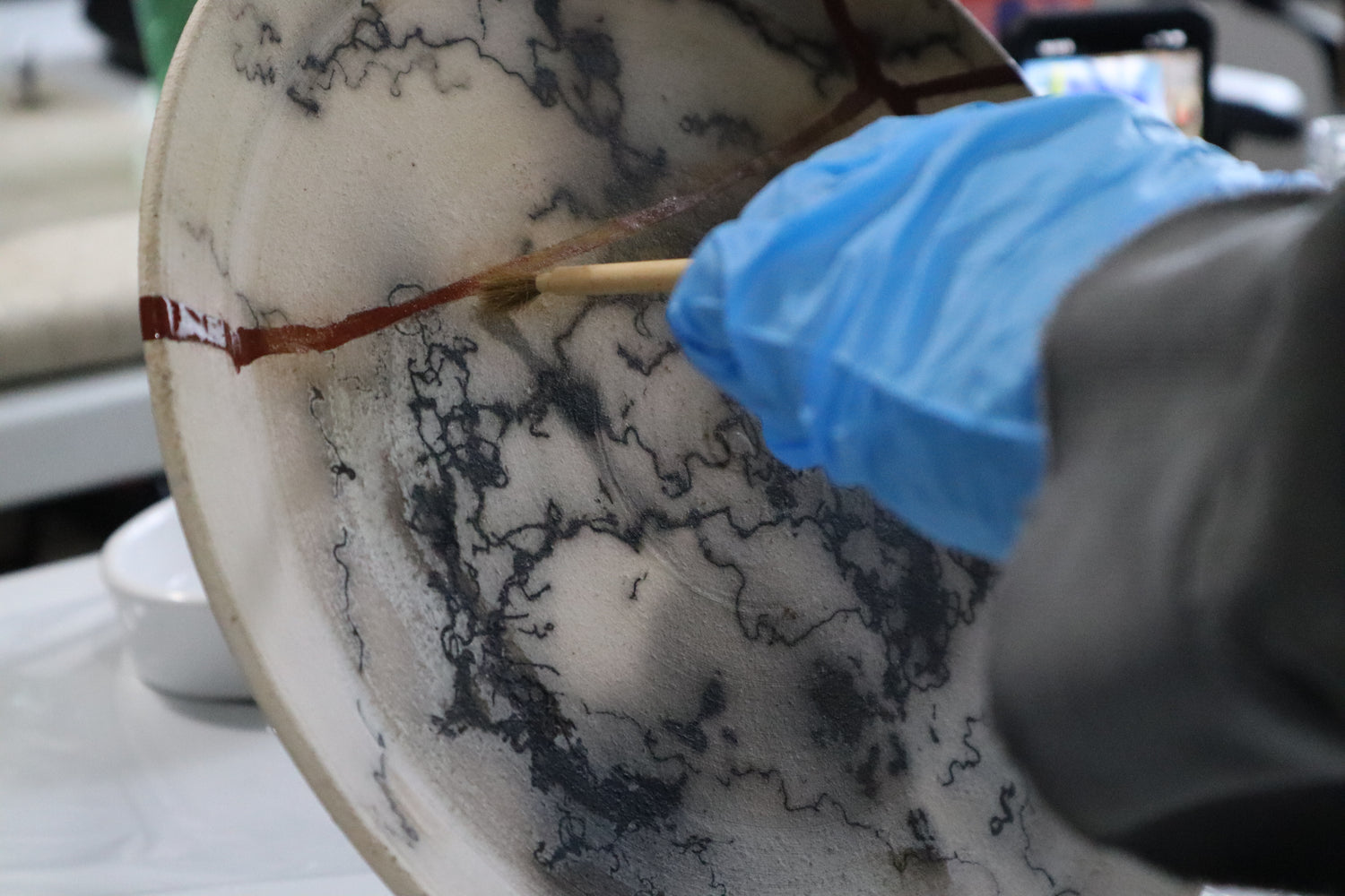 A person with a gloved hand applying gold to a horse hair plate that is being put back together with Kintsugi 