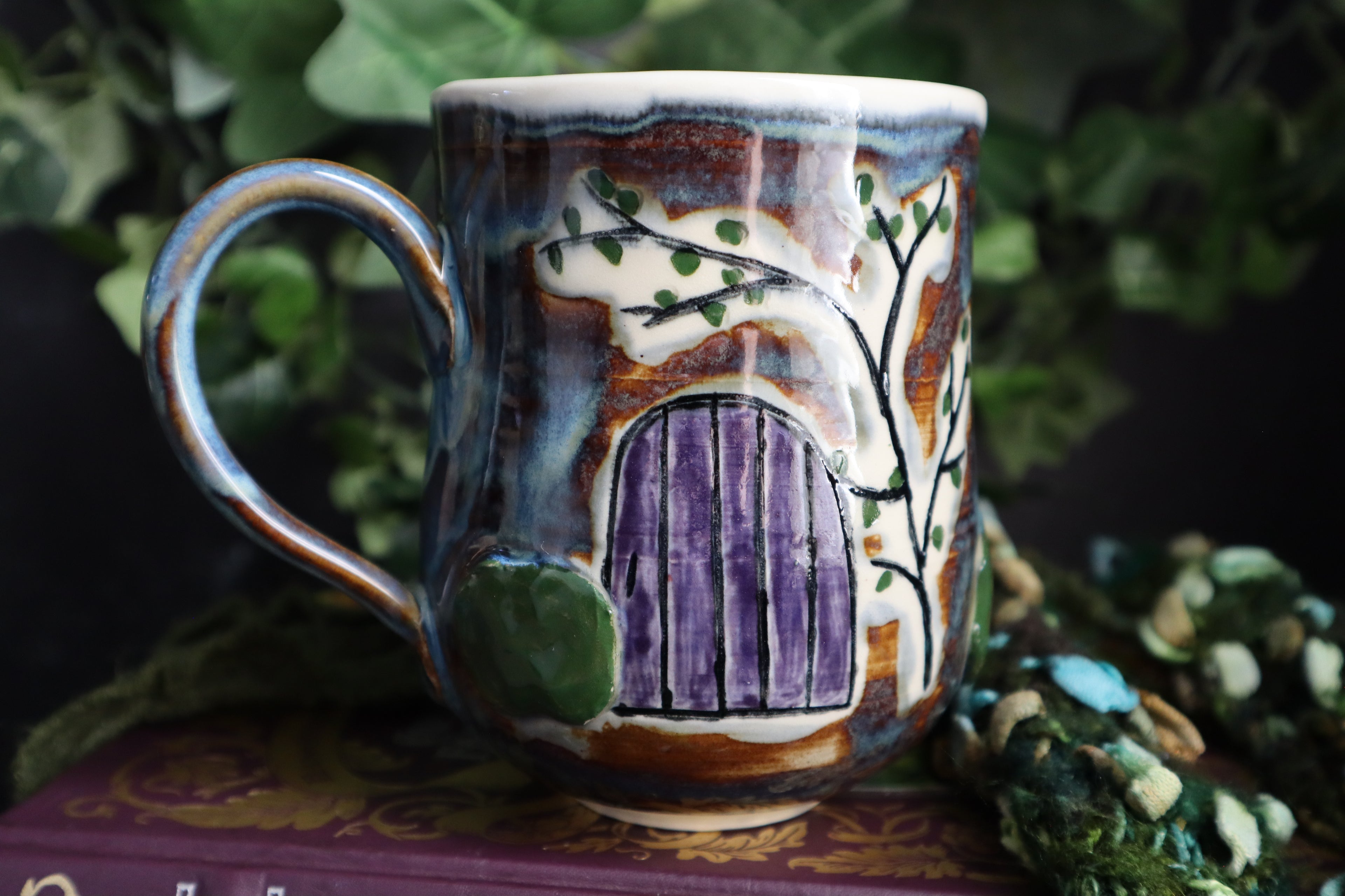 Handcrafted ceramic mug with a decorative design of a purple door and greenery on a dark background.