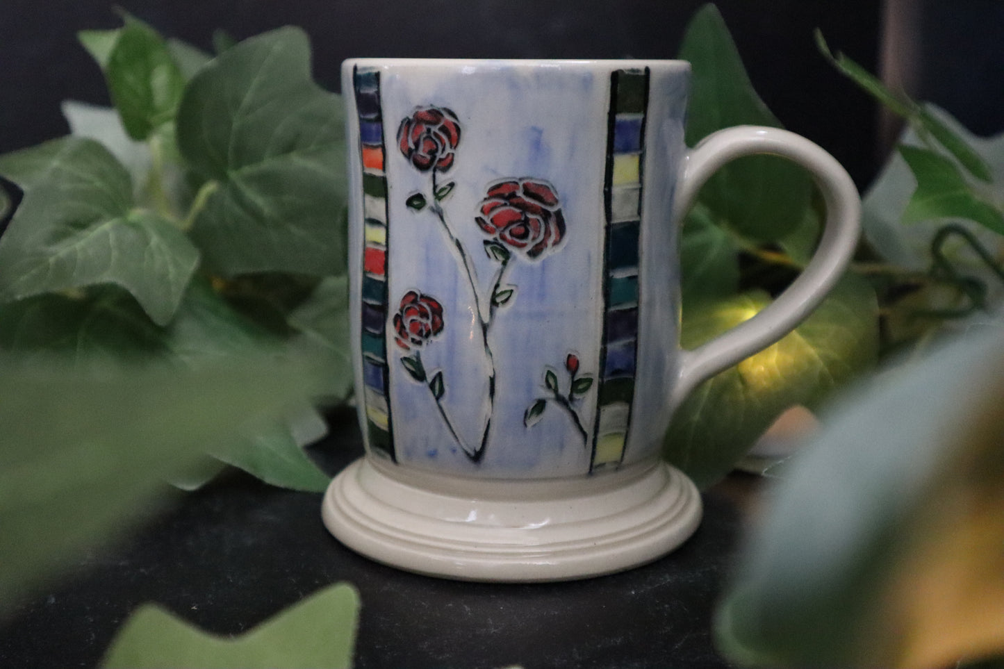 Ceramic mug with floral design on a dark surface with green leaves in the background