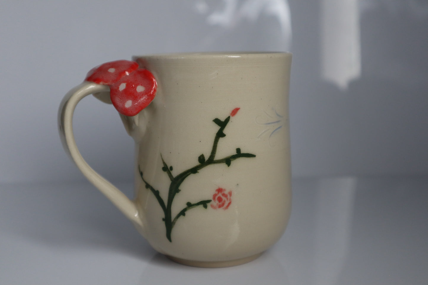 White mug with a mushroom handle and green vines on it with a white backdrop