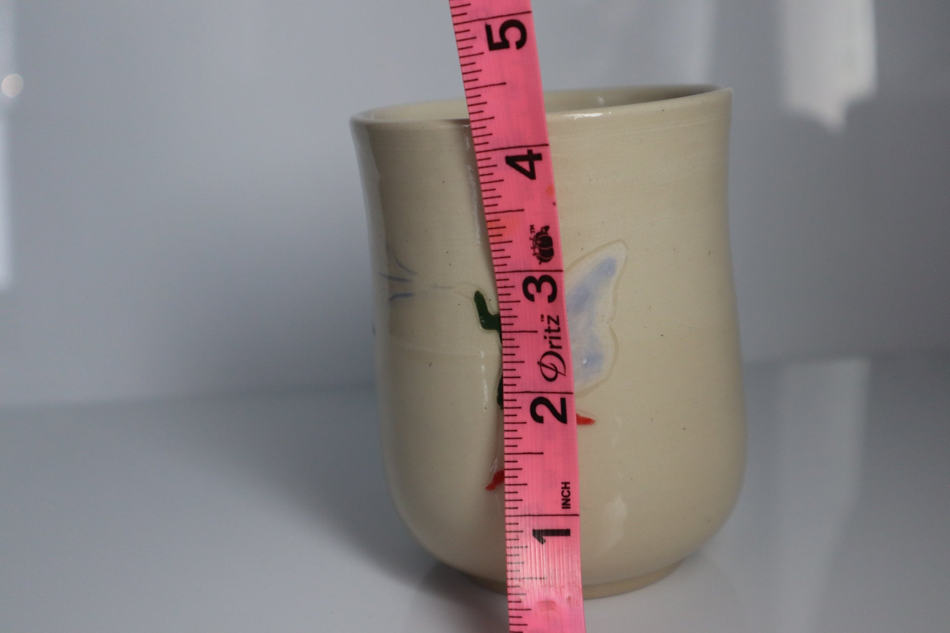 Ceramic mug with a pink measuring tape showing its height against a white background