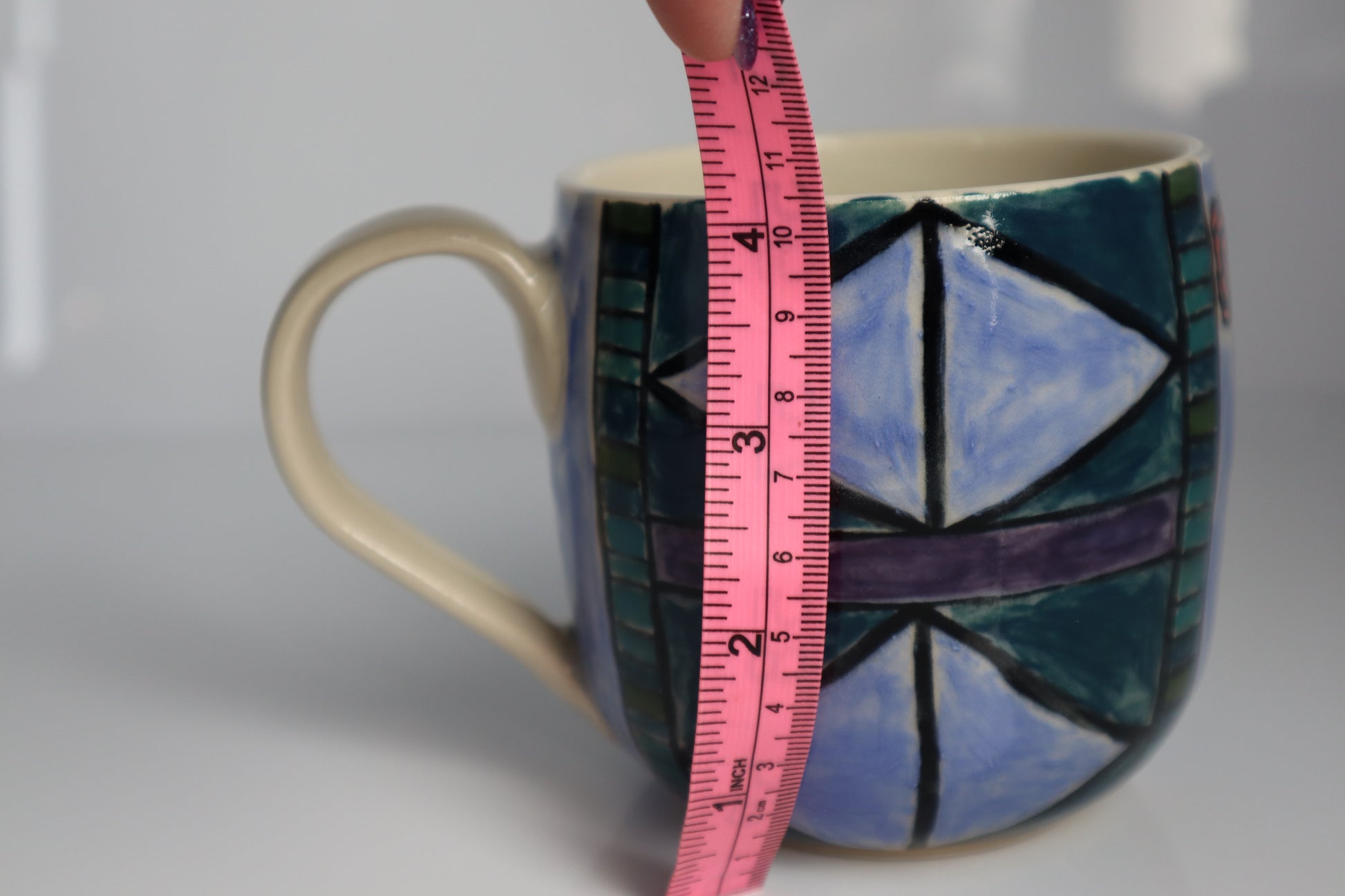 Ceramic mug with a pink measuring tape for scale on a white background