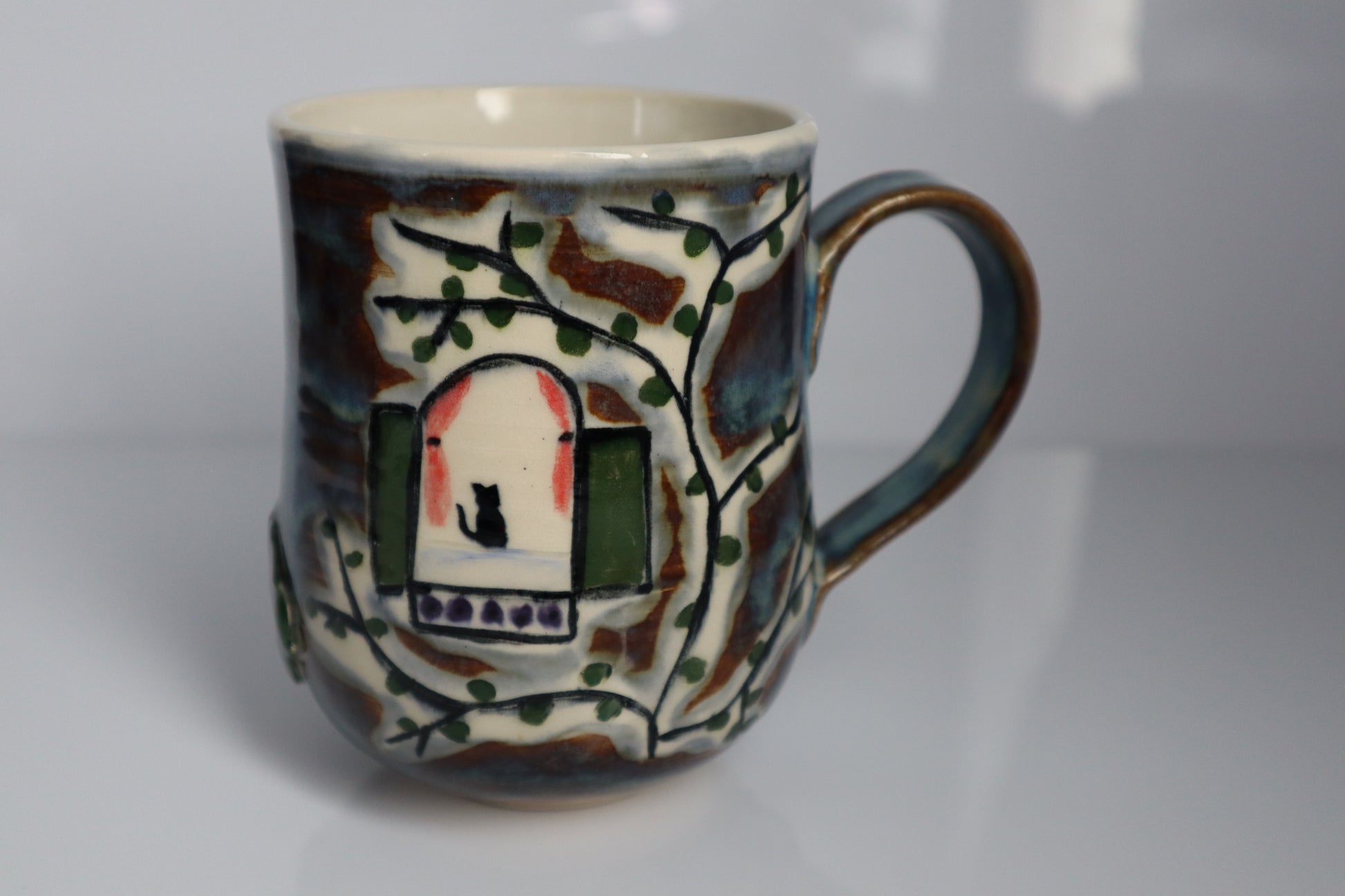 One side of the mug with a vine and a cat sitting in the window on a white background