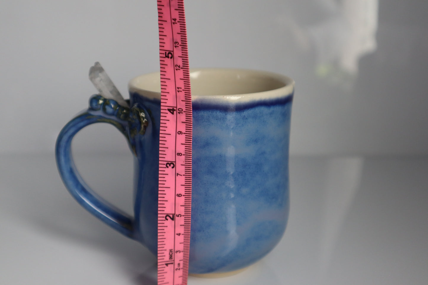 Blue ceramic mug with a measuring tape for scale on a gray background