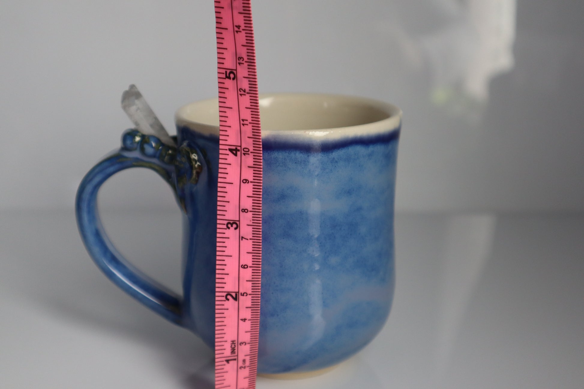 Blue ceramic mug with a measuring tape for scale on a gray background