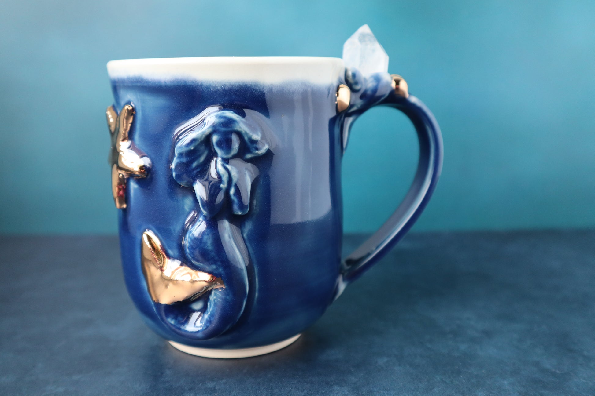 Blue and gold ceramic mug with mermaid design on a blue background
