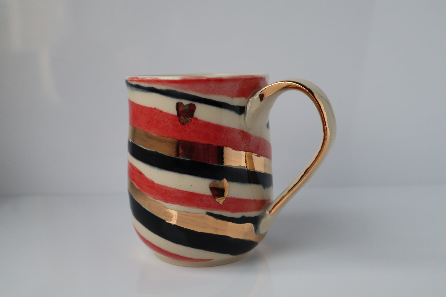 Ceramic mug with red, black, and gold stripes on a white background