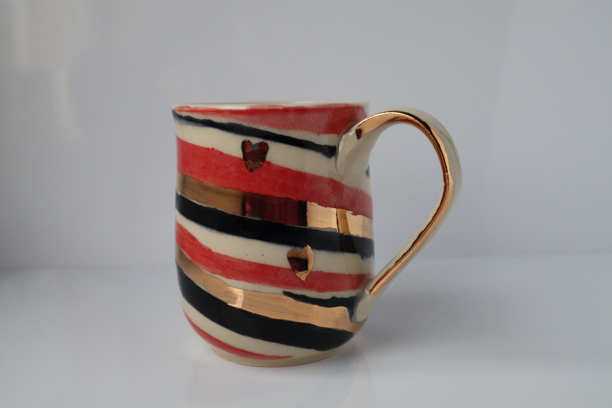 Ceramic mug with red, black, and gold stripes on a white background