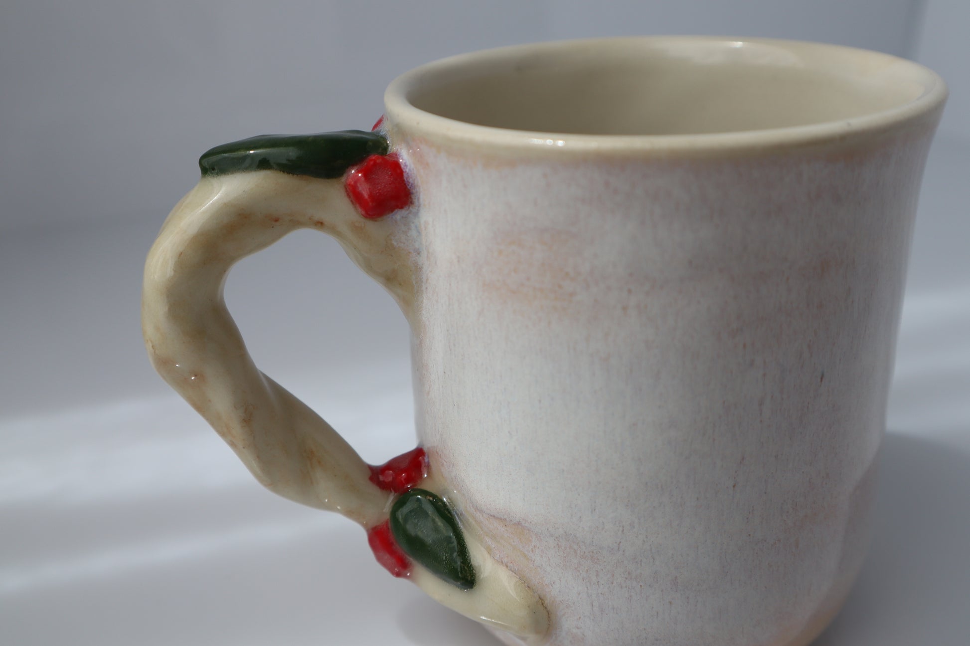 Ceramic mug with decorative handle featuring red flowers and green leaves on a white background