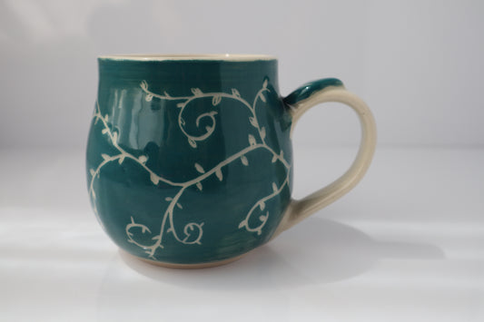 Teal mug with white floral patterns on a white background