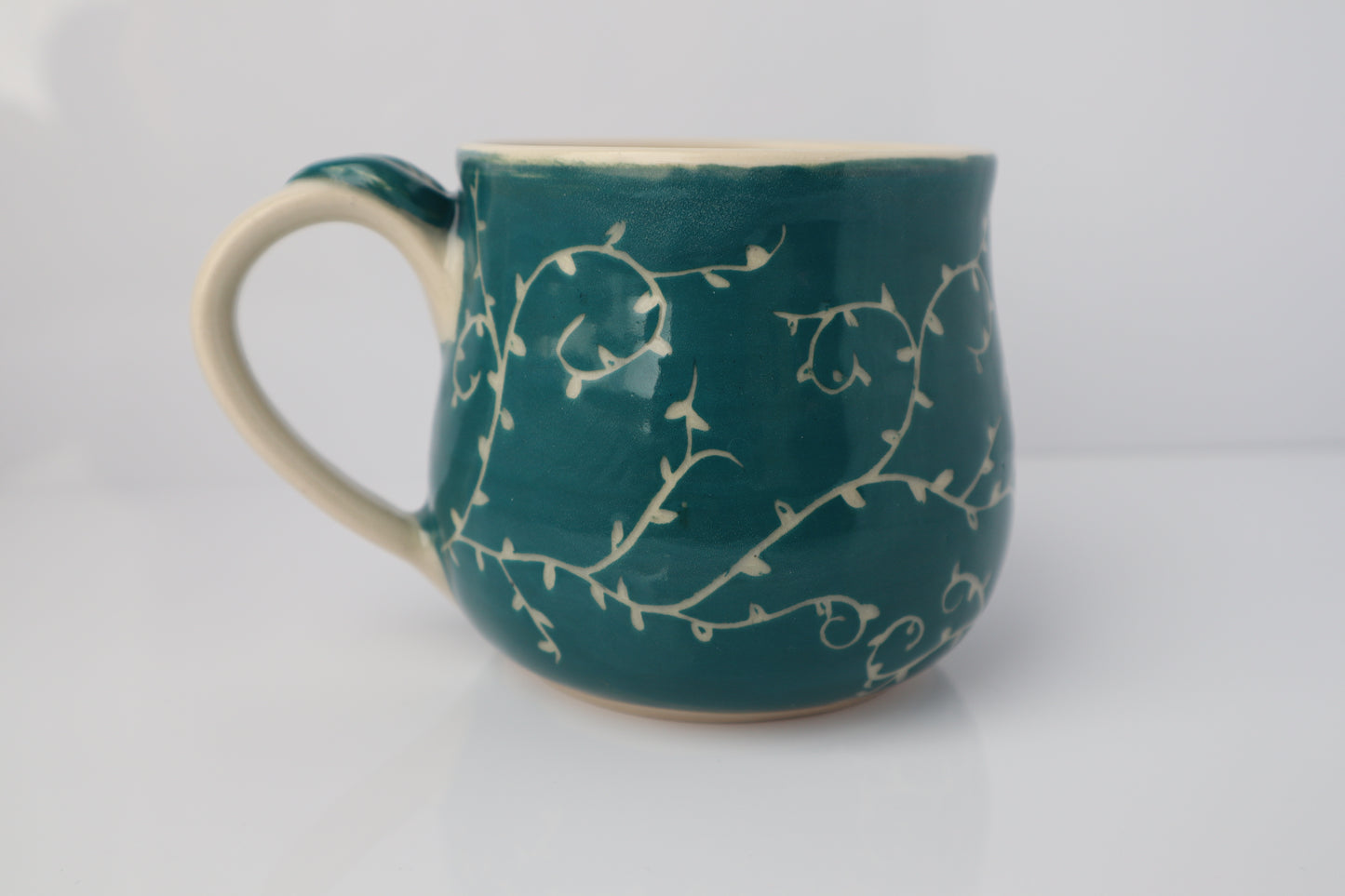 Teal mug with white floral patterns on a white background