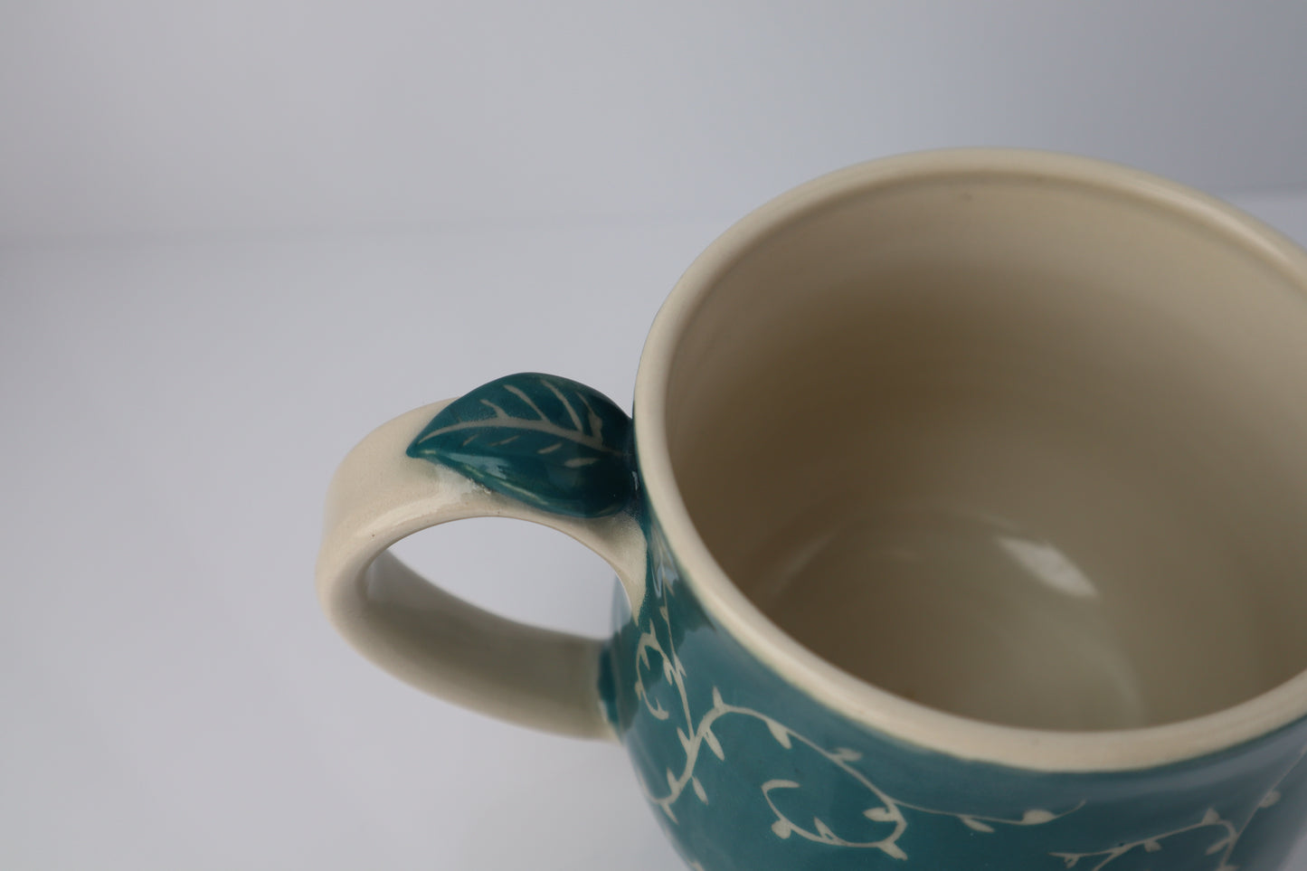Teal mug with leaf handle on a white background