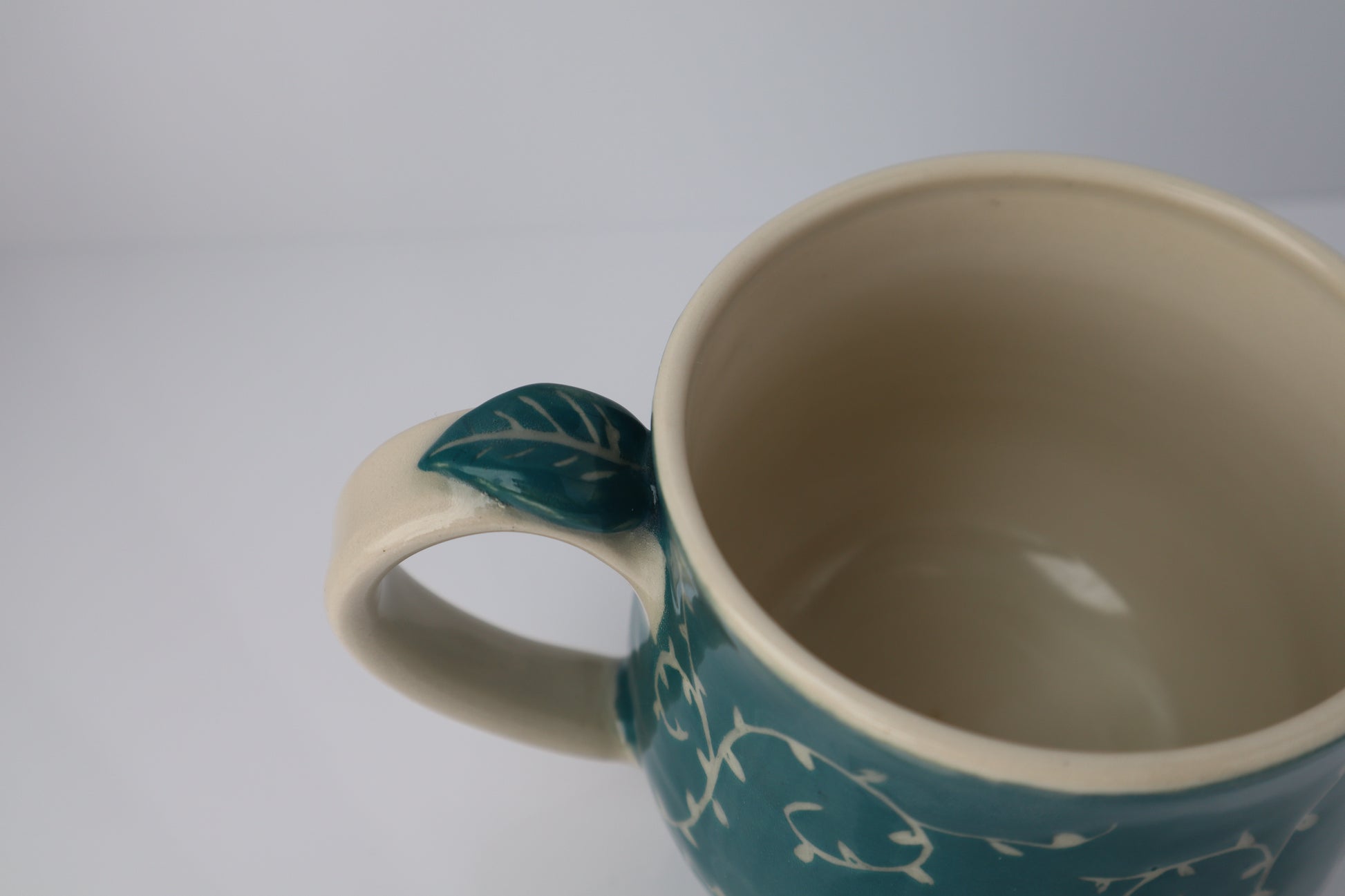 Teal mug with leaf handle on a white background