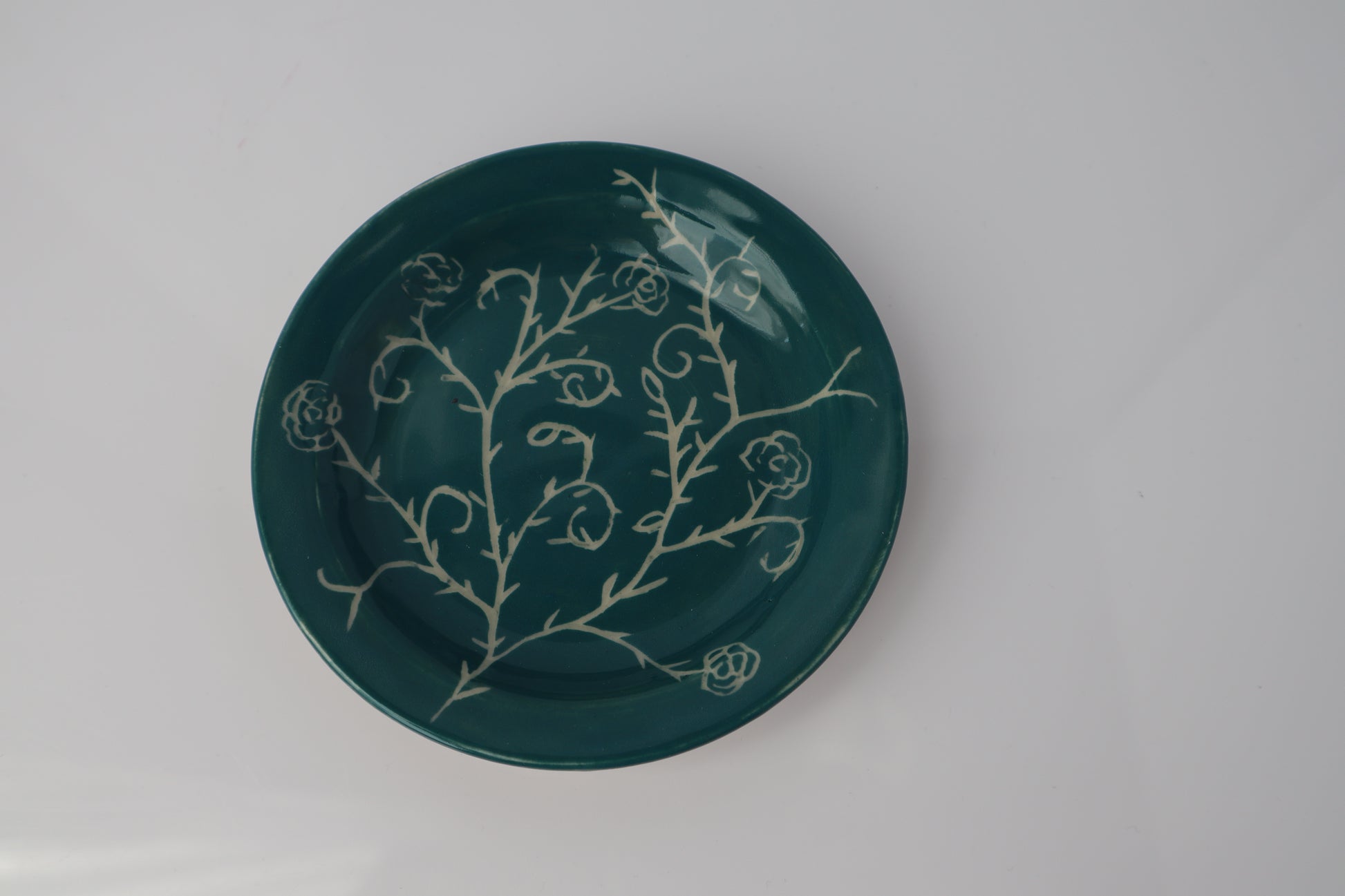 Green ceramic plate with white floral patterns on a gray background