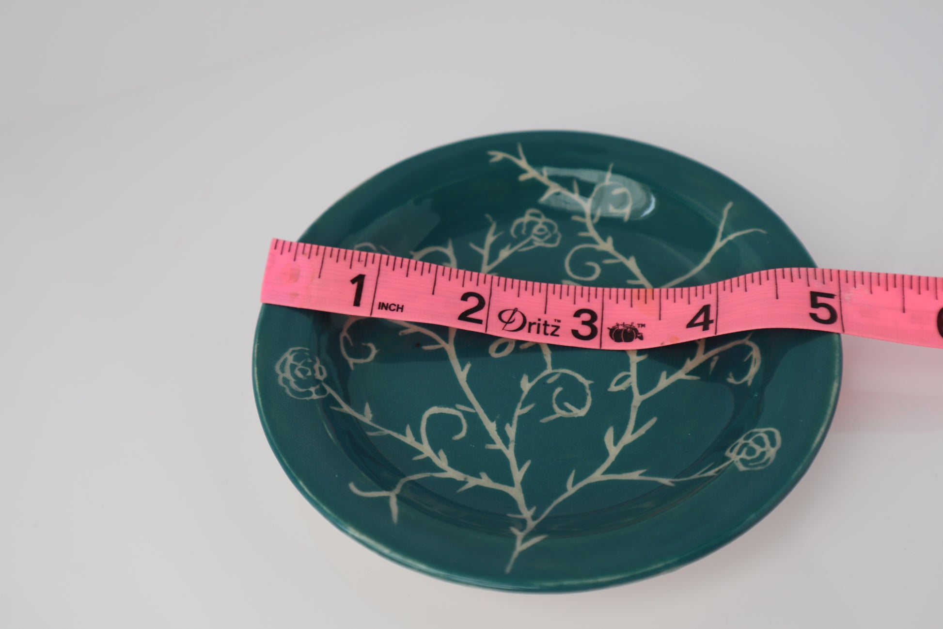 Teal plate with white floral design and a pink measuring tape for scale