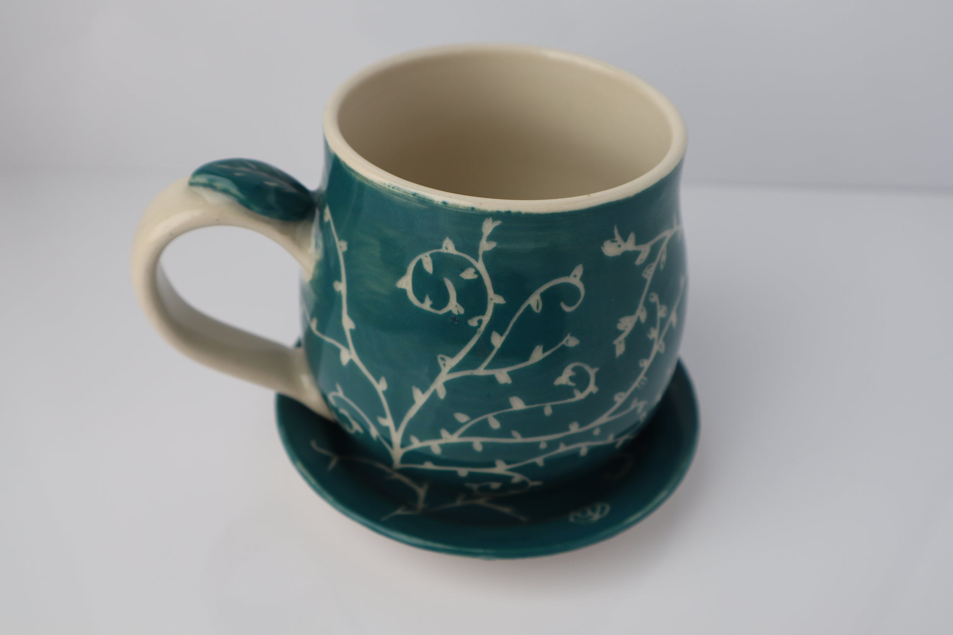 Teal mug with white floral patterns on a matching coaster against a light gray background