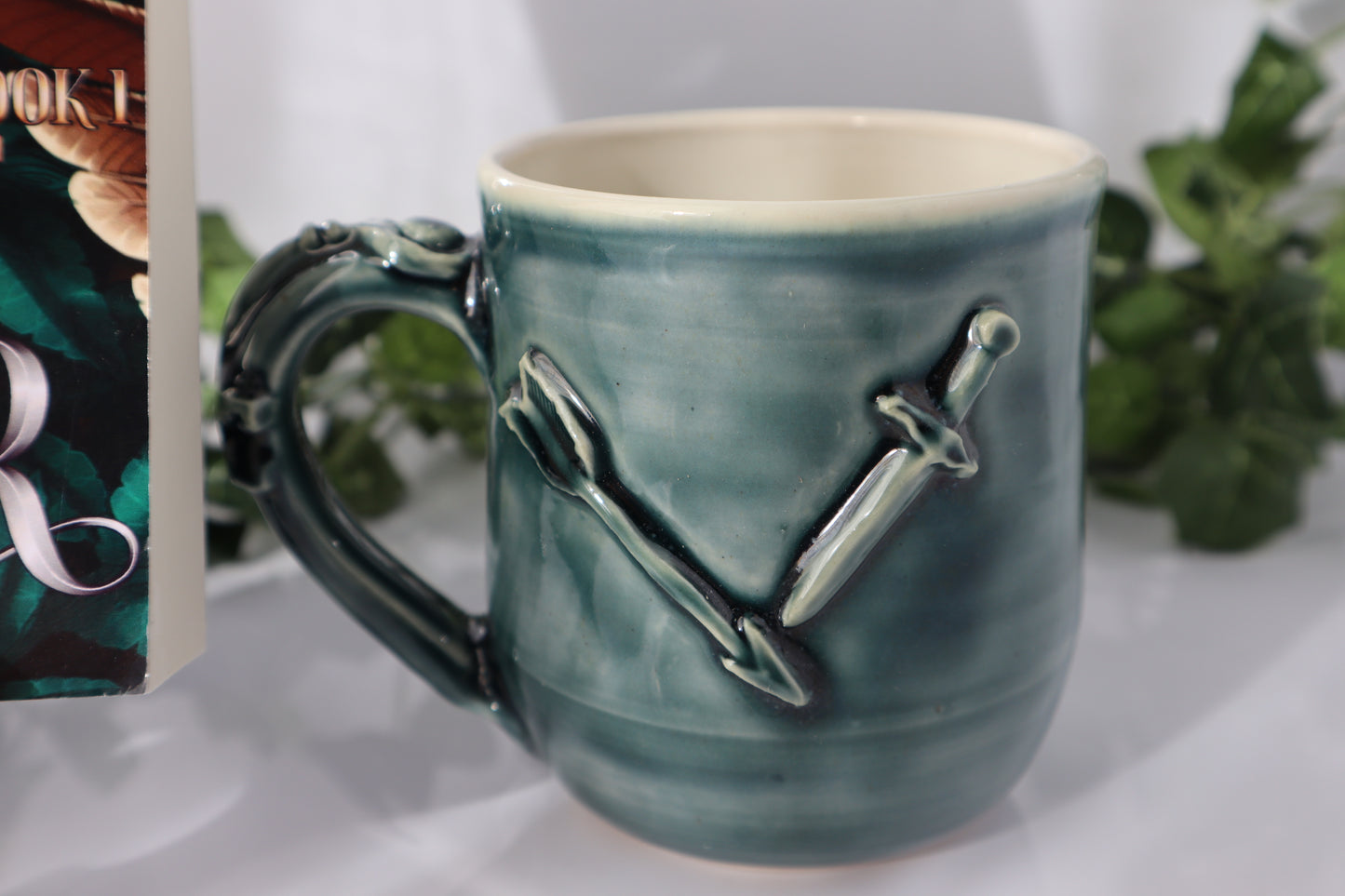 Green ceramic mug with sword and arrow design on a white surface