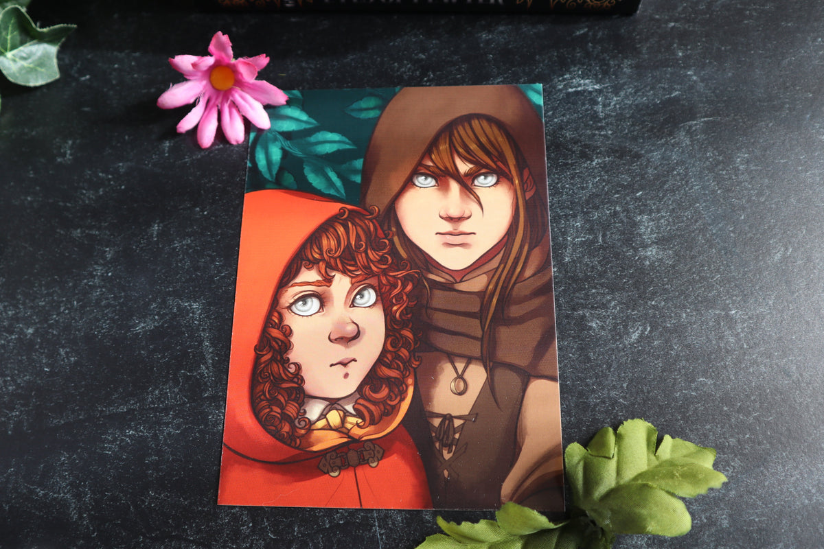 Printed Character art, featuring an illustrated portrait of Kalahn and Piper, placed on a dark textured surface with decorative green leaves and a pink flower around it.