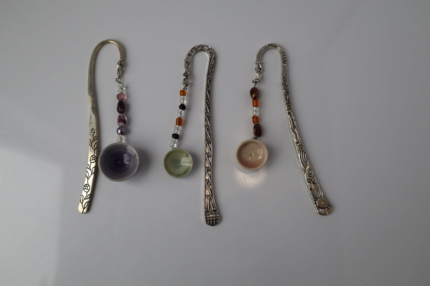 Three decorative bookmarks with ceramic bowl charms on a gray background