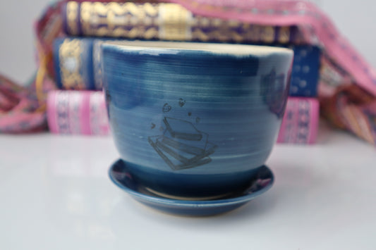 Blue planter with a stack of book designs on it, sitting in front of a stack of books.